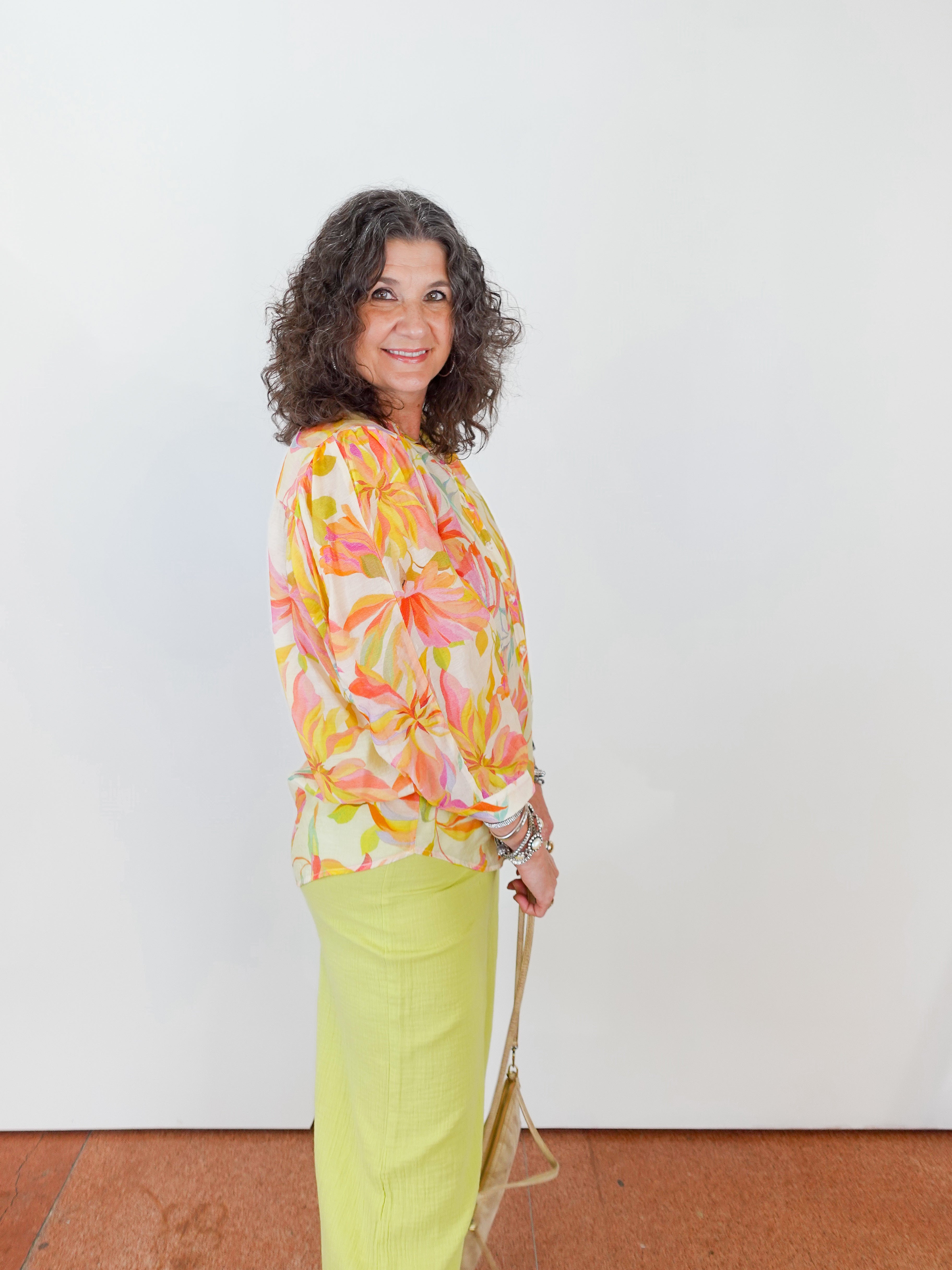 Woman wearing a colorful floral blouse and bright yellow pants against a white background
