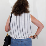 Person wearing a striped sleeveless top and blue jeans against a white background