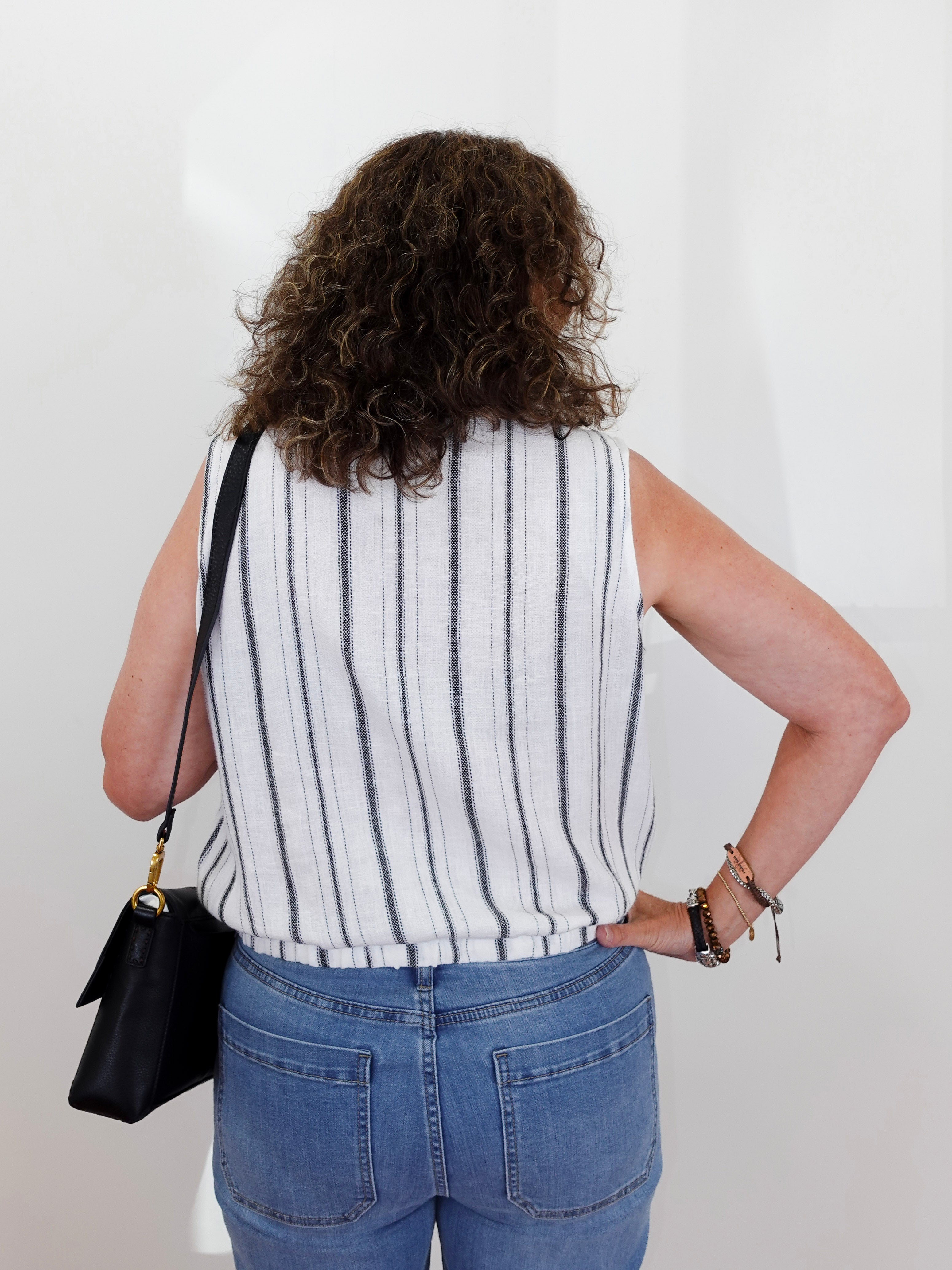 Person wearing a striped sleeveless top and blue jeans against a white background