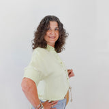 Woman wearing a light green blouse and blue jeans against a white background