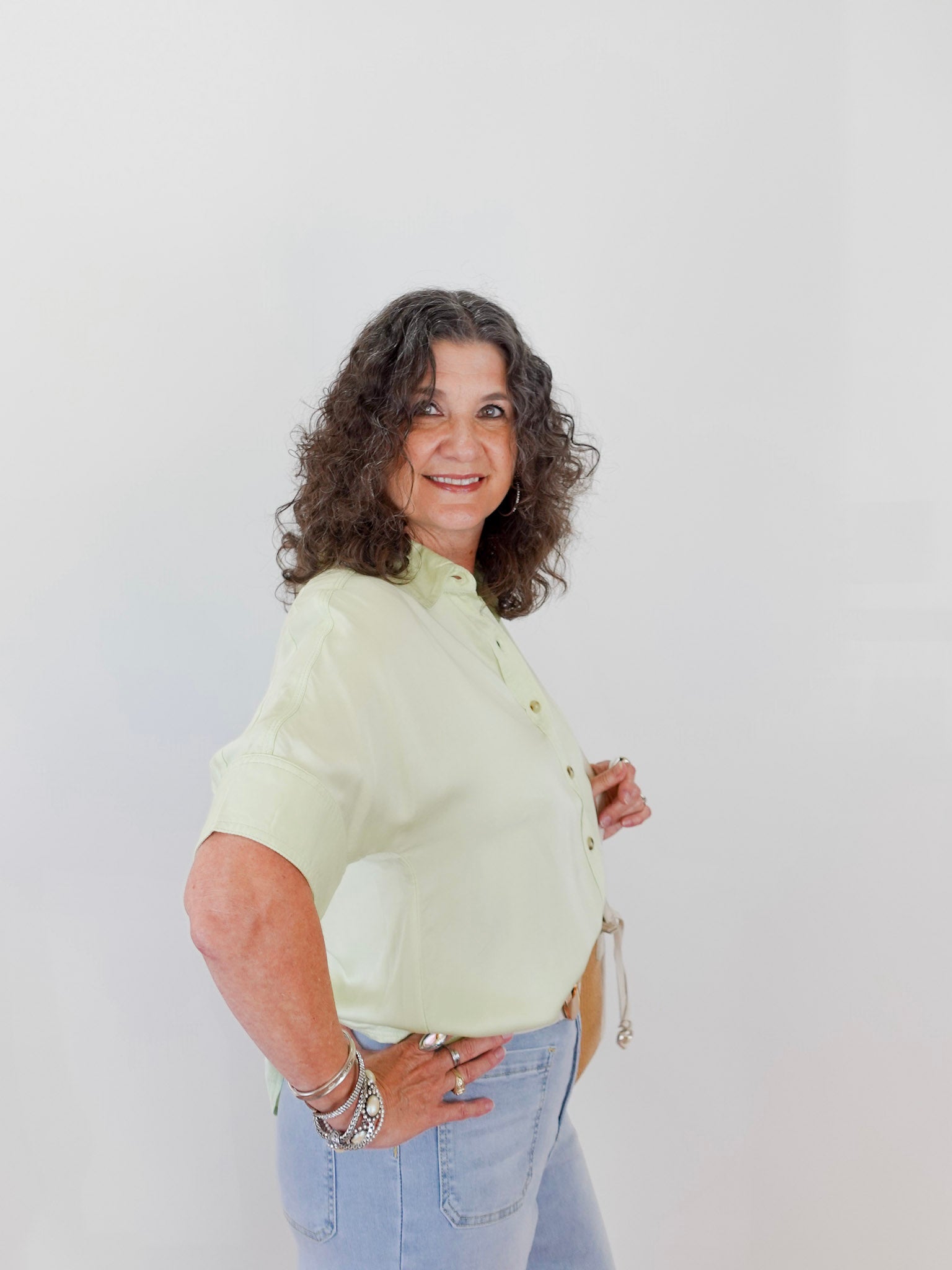Woman wearing a light green blouse and blue jeans against a white background