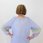 Person wearing a light blue blouse with colorful cuffs and hem on a white background