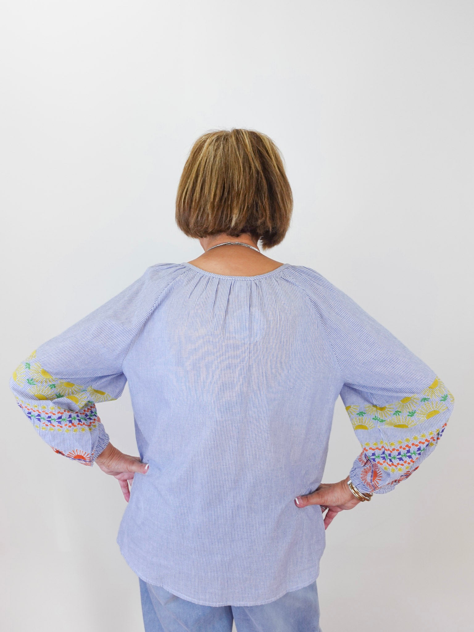 Person wearing a light blue blouse with colorful cuffs and hem on a white background