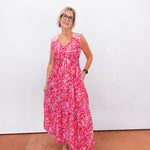 Woman wearing a red floral dress standing against a white wall.