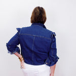 Person wearing a blue denim jacket and white pants on a plain background