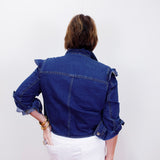 Person wearing a blue denim jacket and white pants on a plain background