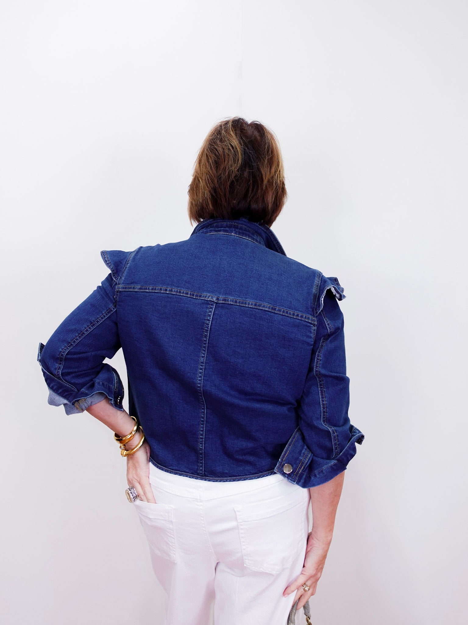 Person wearing a blue denim jacket and white pants on a plain background