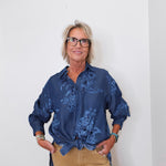 Person wearing a blue patterned shirt and beige pants against a white background