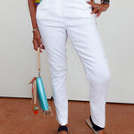 Person wearing white pants and colorful top with a small bag, standing on a brown floor.