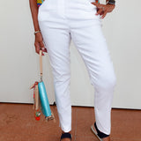Person wearing white pants and colorful top with a small bag, standing on a brown floor.