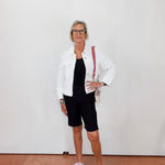 Woman wearing a white jacket, black top, and shorts with white sneakers against a plain background