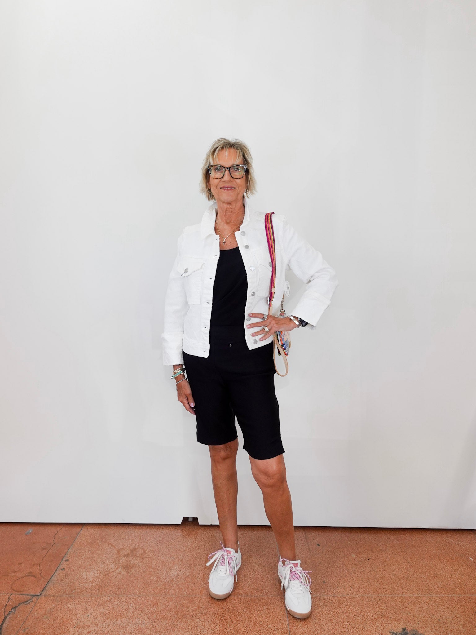 Woman wearing a white jacket, black top, and shorts with white sneakers against a plain background