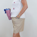 Person wearing a white t-shirt with red, white, and blue designs and beige shorts, holding a patterned bag.