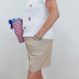 Person wearing a white t-shirt with red, white, and blue designs and beige shorts, holding a patterned bag.