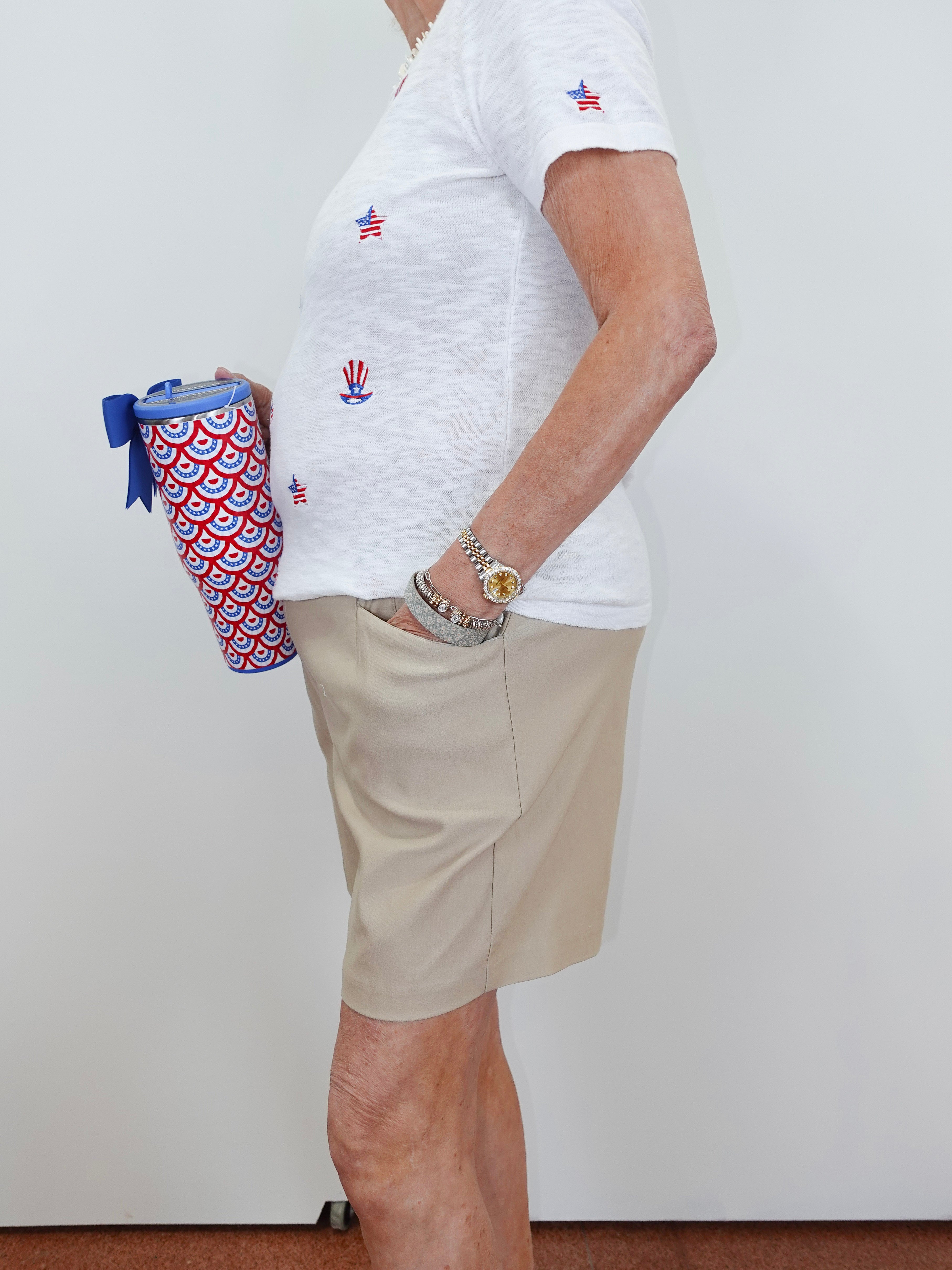 Person wearing a white t-shirt with red, white, and blue designs and beige shorts, holding a patterned bag.