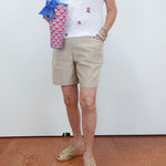 Person wearing a white shirt with colorful patterns, beige shorts, and open-toe sandals, holding a patterned bag.