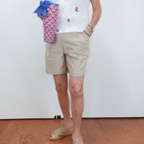 Person wearing a white shirt with colorful patterns, beige shorts, and open-toe sandals, holding a patterned bag.