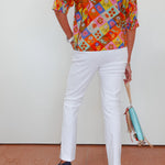 Person wearing a colorful patterned shirt and white pants, holding a blue bag on a white background.