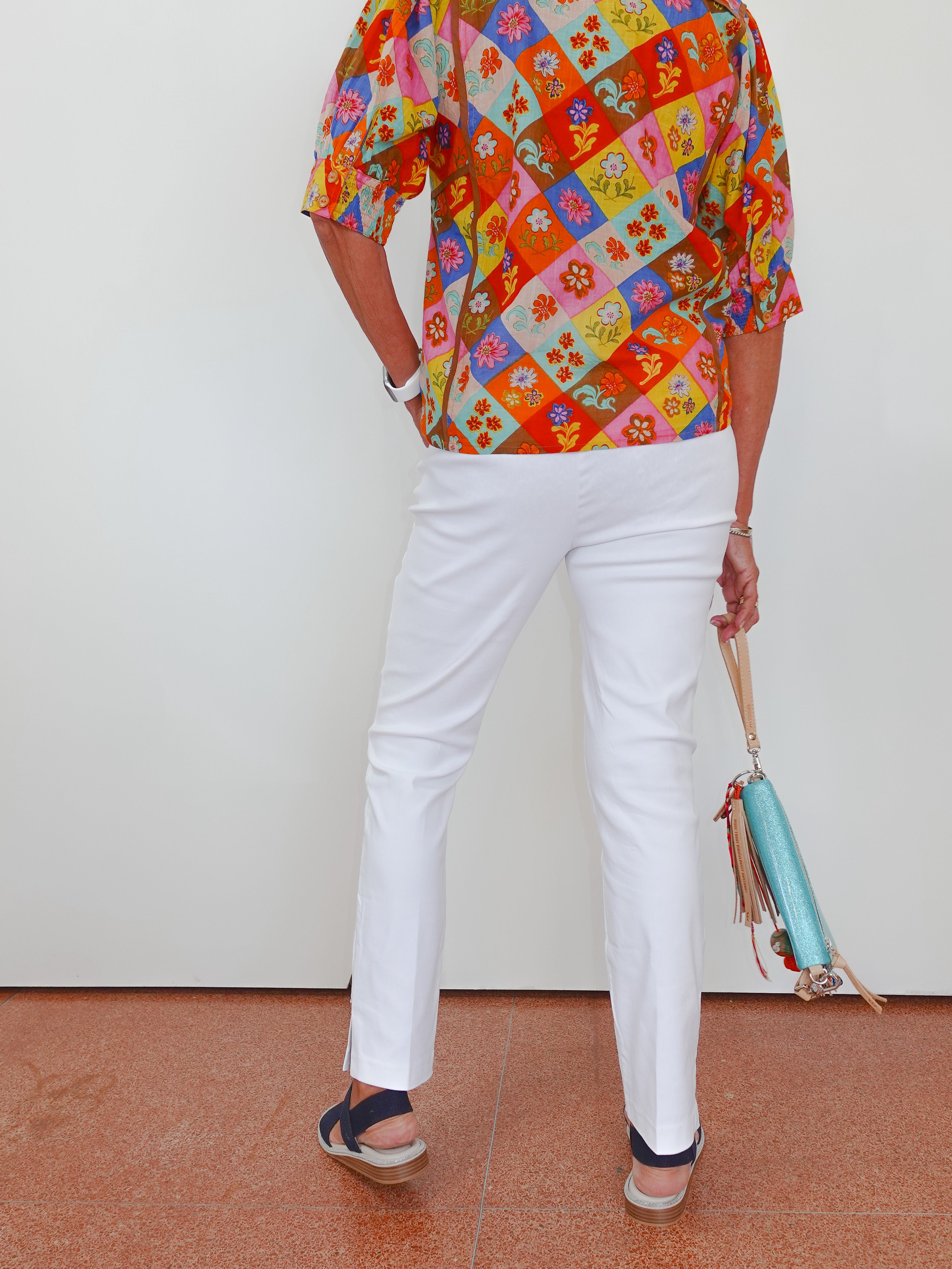 Person wearing a colorful patterned shirt and white pants, holding a blue bag on a white background.