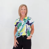 Woman wearing a colorful patterned shirt and black shorts with a green bag against a white background