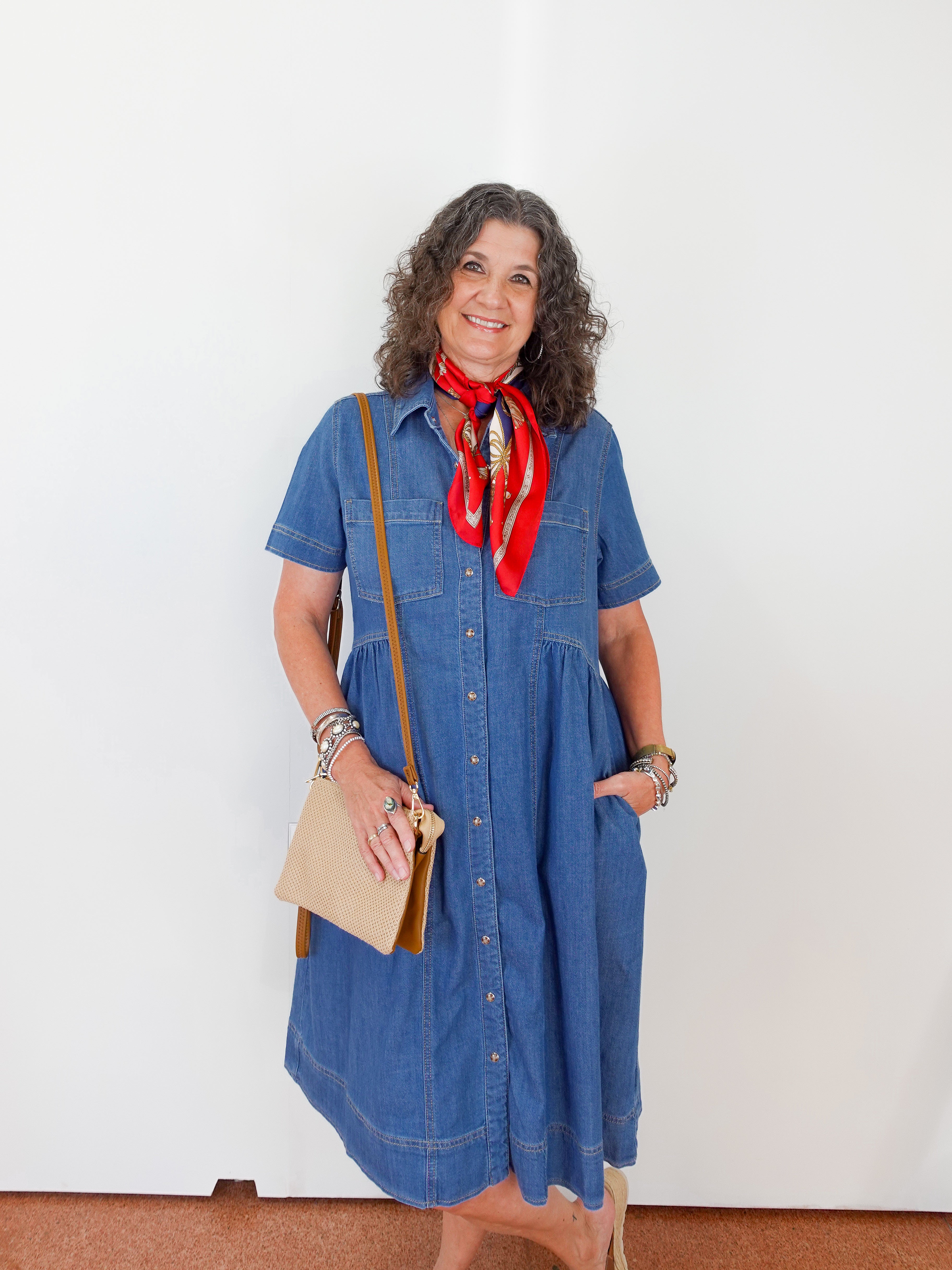 Woman wearing a blue dress with a red scarf and carrying a beige bag against a white background
