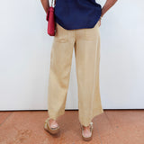 Person wearing a navy blue shirt with embroidery and beige pants, standing against a white wall.