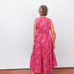 Woman wearing a red floral dress standing against a white wall.