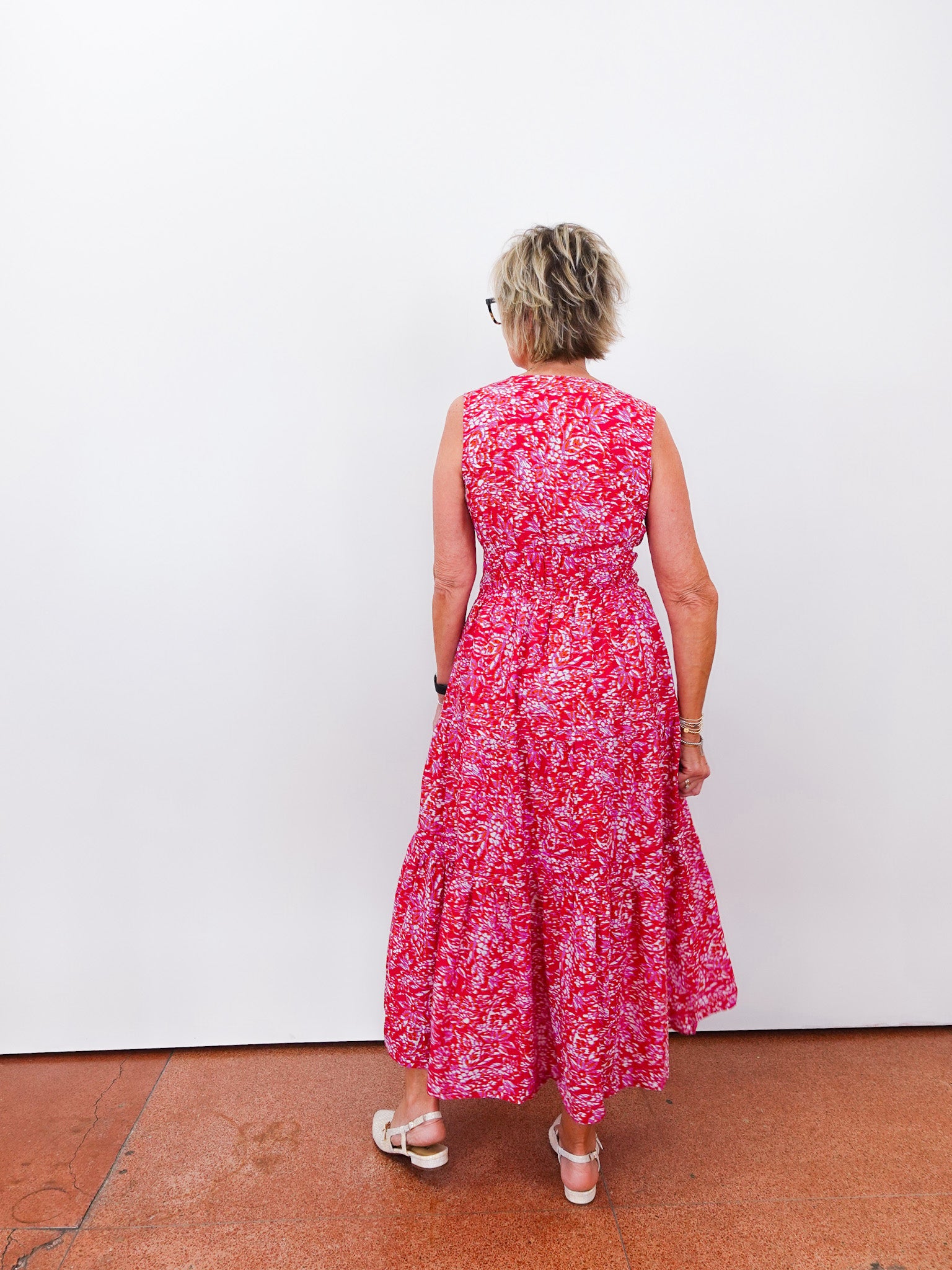 Woman wearing a red floral dress standing against a white wall.