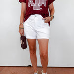 Person wearing a maroon t-shirt with a logo and white shorts against a white background