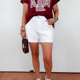 Person wearing a maroon t-shirt with a logo and white shorts against a white background