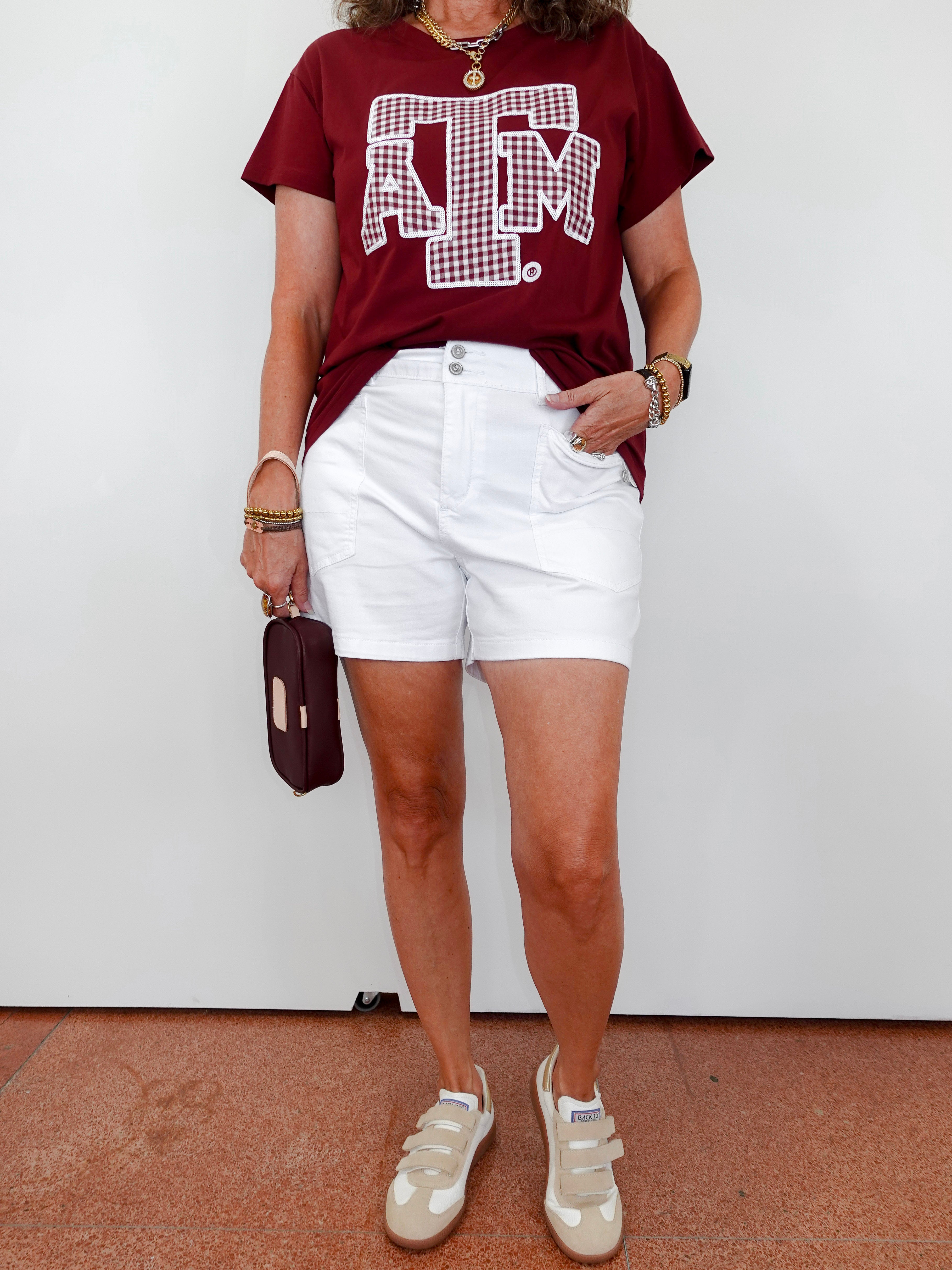 Person wearing a maroon t-shirt with a logo and white shorts against a white background