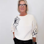 Person wearing a white sweater with black floral designs on a plain background