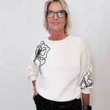 Person wearing a white sweater with black floral designs on a plain background