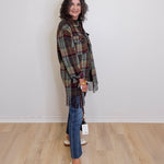 Woman wearing a plaid shawl, jeans, and white sneakers against a plain background