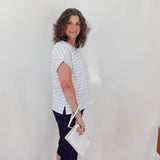 Woman wearing a striped shirt and dark pants holding a white clutch against a plain background