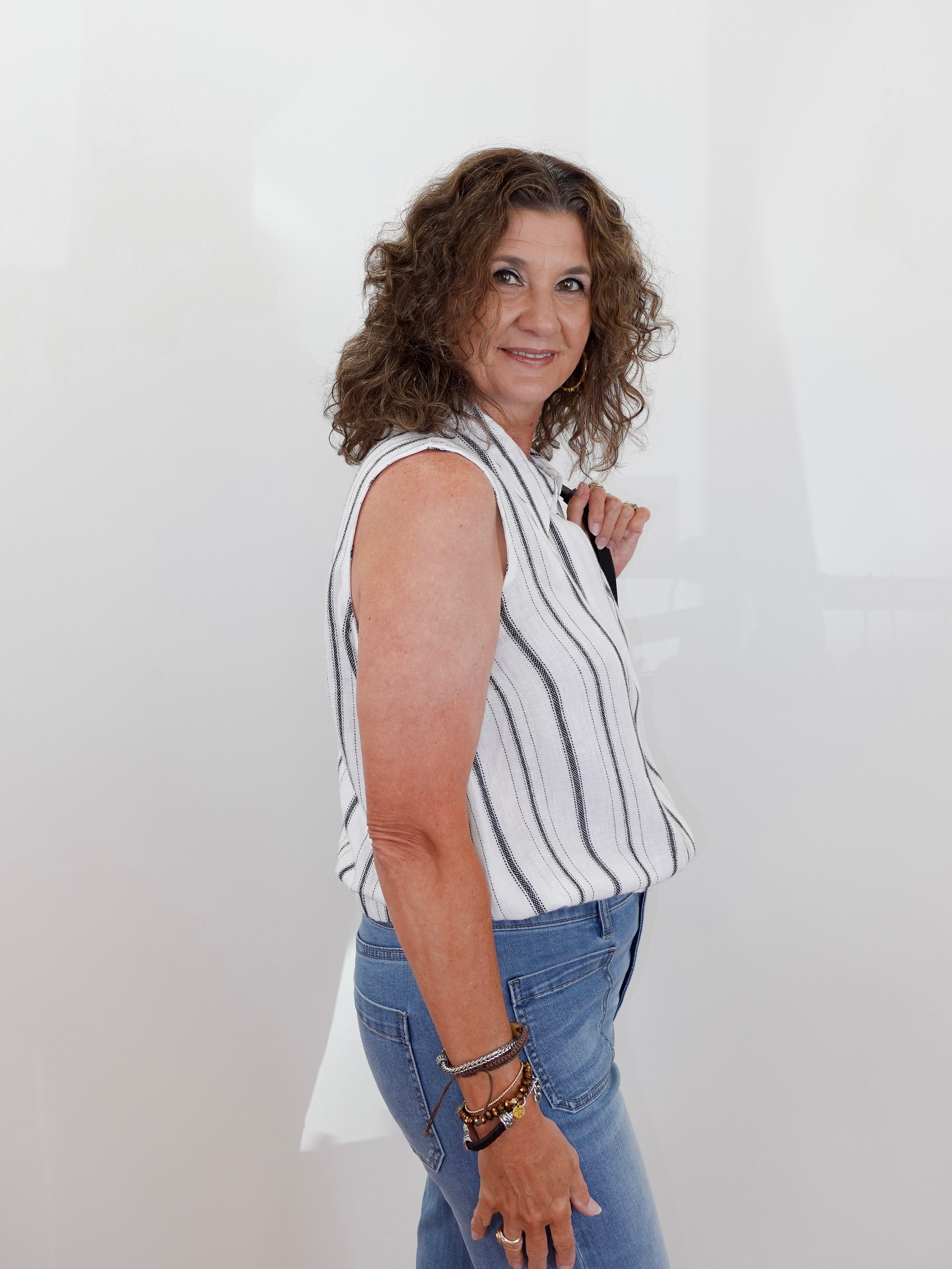 Woman wearing a striped sleeveless top and blue jeans against a white background