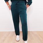 Person wearing teal sweatshirt and pants with white sneakers on a light wooden floor.