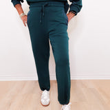 Person wearing teal sweatshirt and pants with white sneakers on a light wooden floor.