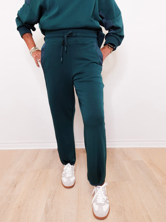 Person wearing teal sweatshirt and pants with white sneakers on a light wooden floor.