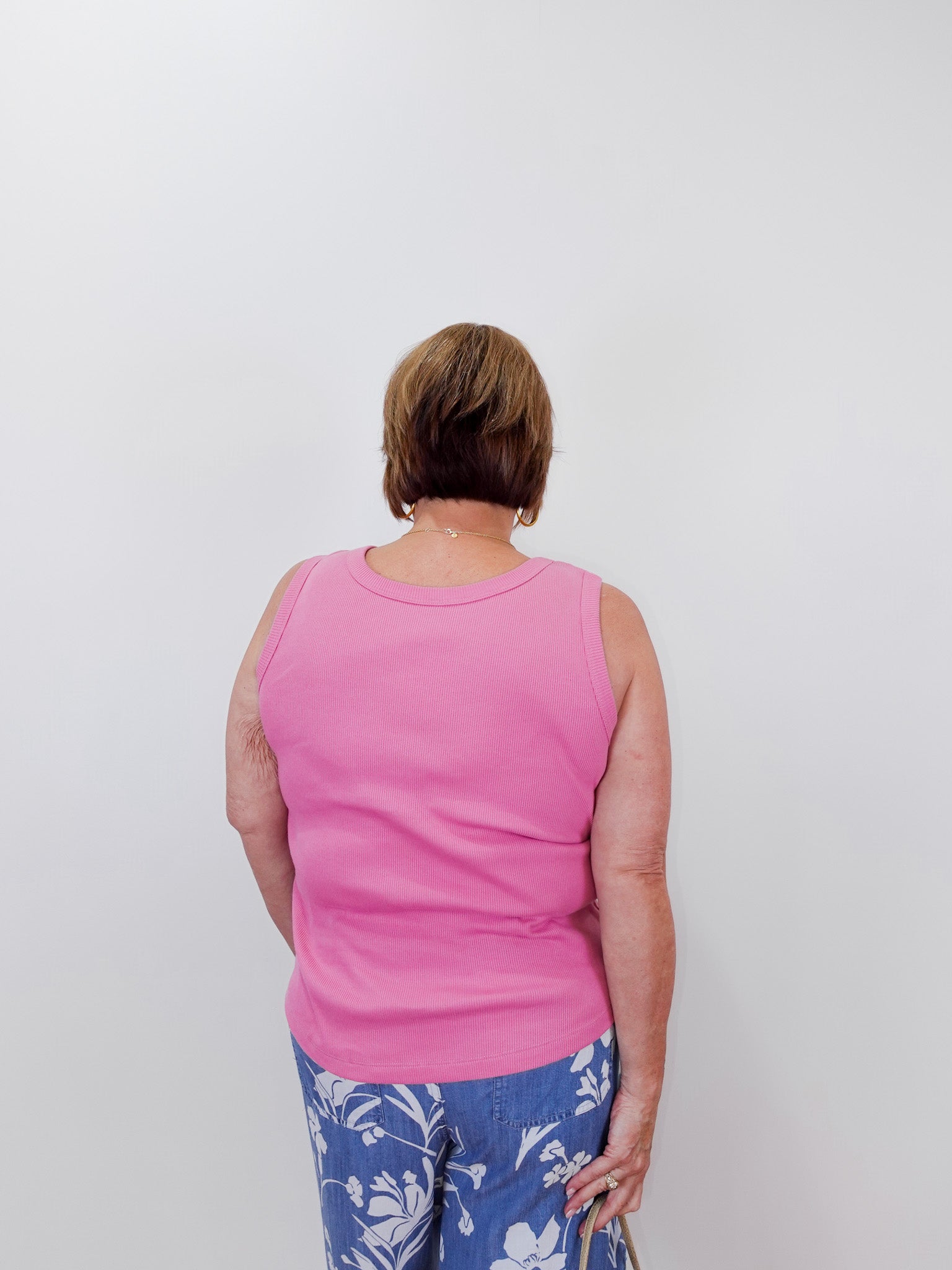 Person wearing a pink tank top and blue floral pants against a white background