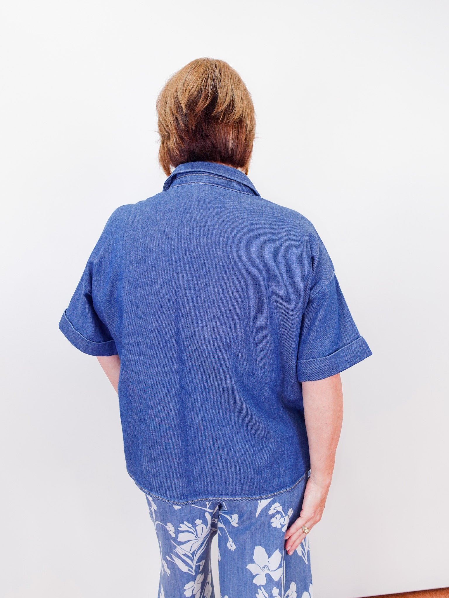 Person wearing a blue shirt and floral pants against a white background