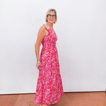 Woman wearing a red floral dress standing against a white wall.