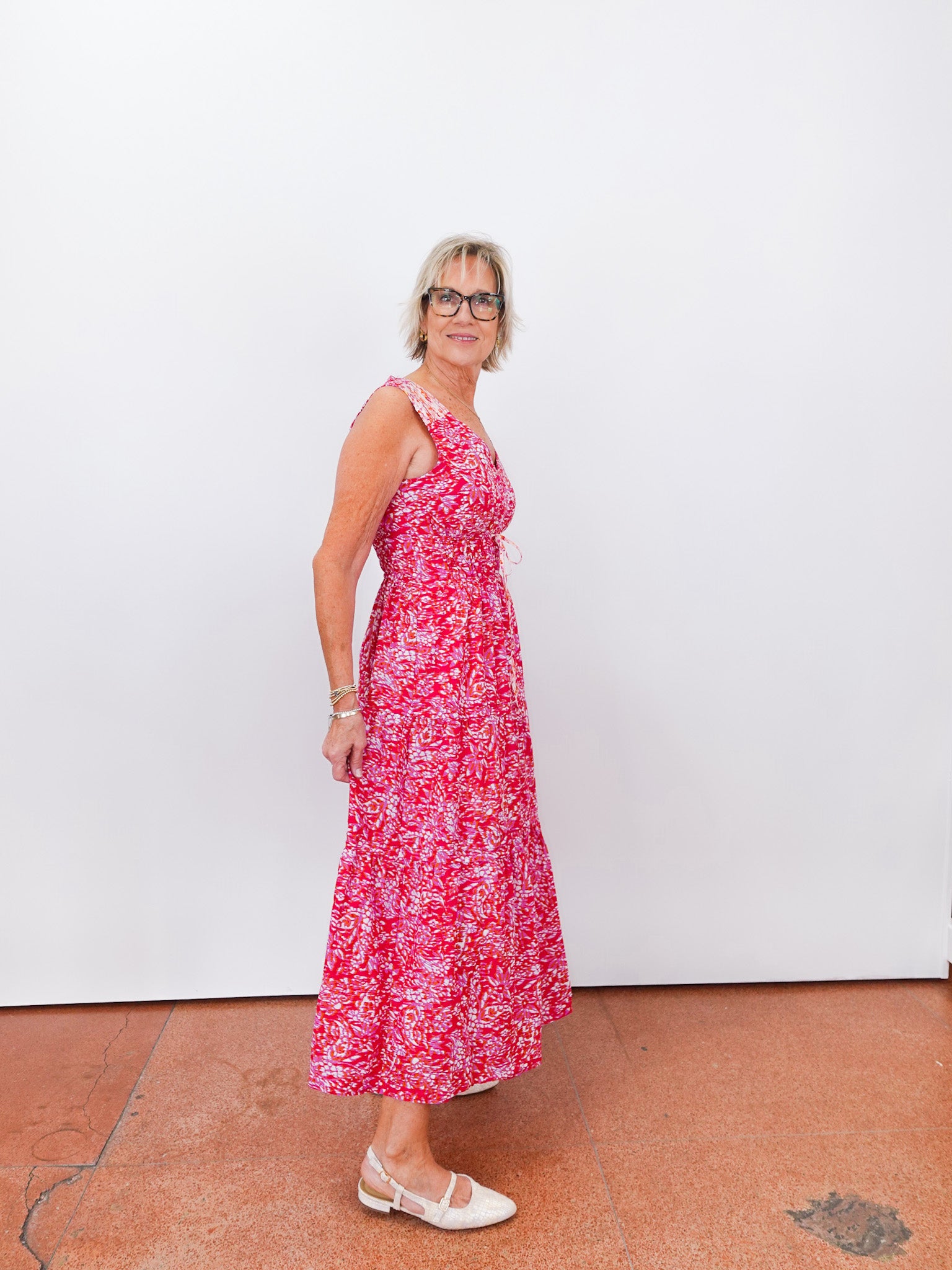 Woman wearing a red floral dress standing against a white wall.