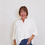 Woman wearing a white blouse and blue jeans against a plain background
