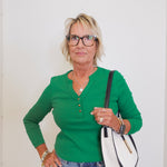 Woman wearing a green sweater and blue jeans, holding a white and black handbag against a white background.