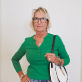 Woman wearing a green sweater and blue jeans, holding a white and black handbag against a white background.