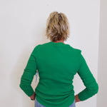 Person wearing a green sweater and blue jeans against a white wall