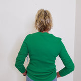 Person wearing a green sweater and blue jeans against a white wall