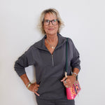 Woman wearing a gray zip-up sweatshirt and black pants against a white background