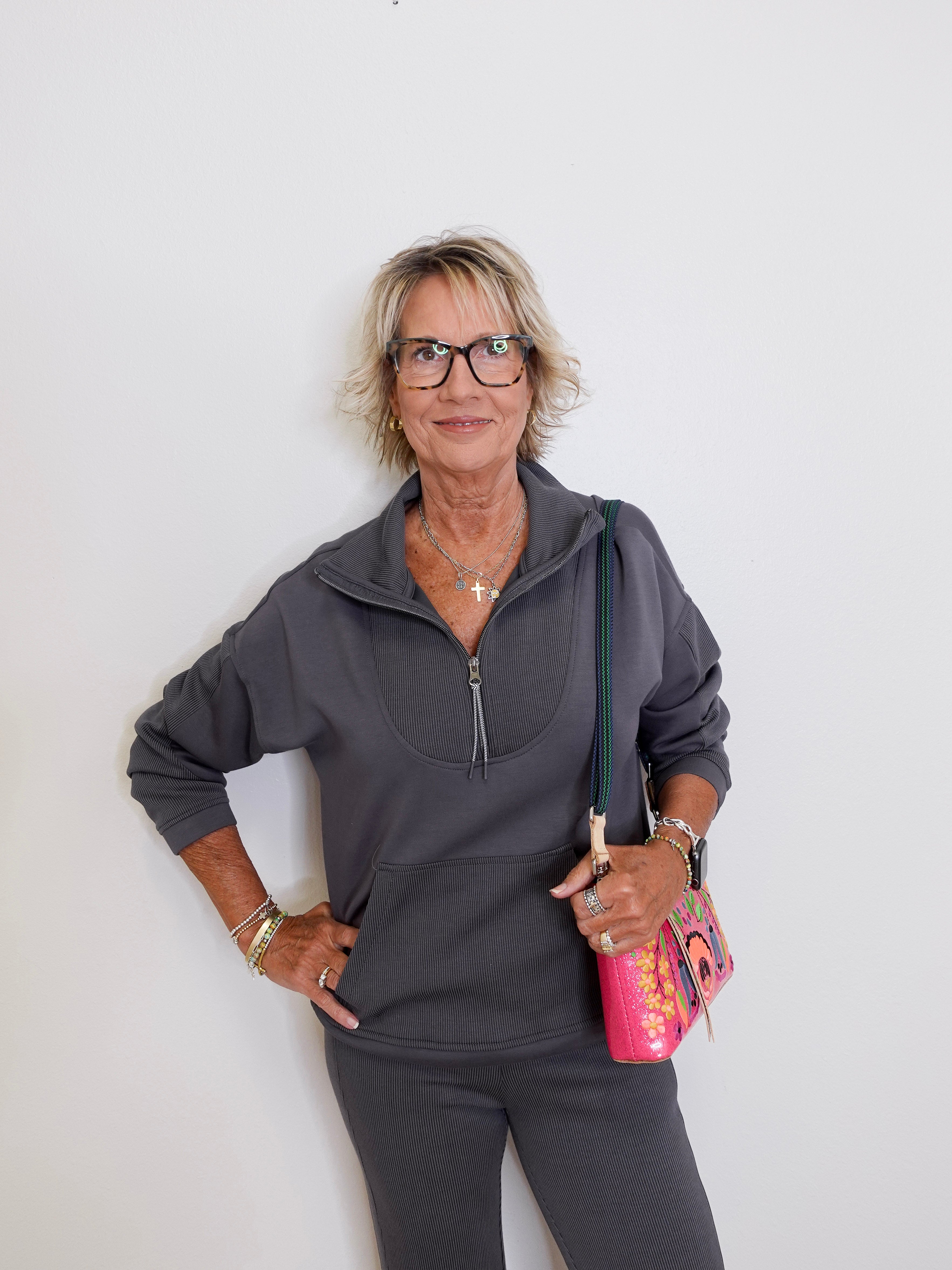 Woman wearing a gray zip-up sweatshirt and black pants against a white background